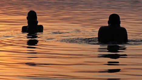 Schöne-Filmische-Aufnahme-Von-Menschen,-Die-Während-Der-Sonnenaufgangszeit-Im-Heiligen-Fluss-Ganga-In-Varanasi-Baden-Und-Das-Wasser-Gold-Glänzen-Lassen