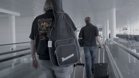 Mann-Mit-Gitarre-In-Gigbag-Und-Gepäck,-Der-An-Der-Flughafenpassage-Spaziert
