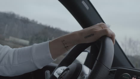 Driver-behind-steering-wheel-inside-modern-car,-tattooed-hand-close-up