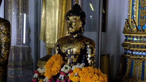 Flowers-Surround-Buddha-Figure-At-A-Temple,-TILT-UP