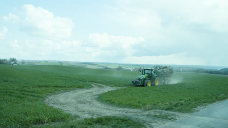 Tractor-driving-manure-on-field-across-dirt-road