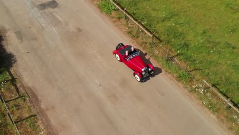 Red-1939-Morgan-4-4-'Le-Mans'---driver-+-passenger-drone-view-side-on---4K---open-top-sports-car-in-English-countryside