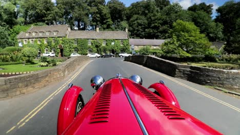 Roter-1939-Morgan-4-4-&#39;Le-Mans&#39;---Blick-Auf-Die-Motorhaube,-Der-über-Die-Brücke-Geht---Slomo---Offener-Sportwagen-In-Englischer-Landschaft-An-Einem-Perfekten-Tag