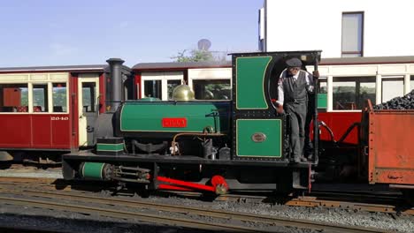 Ffestiniog-Railway---engineer-shunts-LILLA-narrow-gauge-steam-engine-forwards-with-truckloads-of-coal,-Porthmadog-Harbour-Railway-Station,-Snowdonia,-Wales---man-in-cap,-SLOMO-60fps