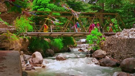 Cinematic-Slo-Mo-shot-of-people-crossing-bridge-over-Ganges-river-crystal-clear-water-flowing-downstream-from-mountains-in-harshal-village-of-uttarakhand