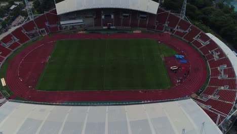 Thammasat-University-main-stadium-bird’s-eye-view-by-drone-zoom-in-to-the-field,-stand-and-race-track,-Thailand