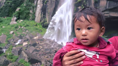 Mother-holding-cute-kid-during-their-visit-to-jogini-waterfall,-manali