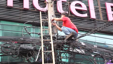 Young-Asian-Male-Fixing-A-Wire-Across-A-Street,-Climbs-Down-Ladder