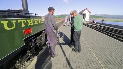 Steam-train-engineer-and-fireman-chat-with-train-enthusiasts-alongside-LYD-narrow-gauge-steam-engine-,-Ffestiniog-Railway-,Porthmadog-Harbour-Railway-Station,-Snowdonia,-Wales---SLOMO-60fps