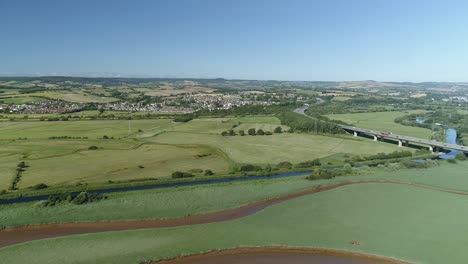 Expansive-farmland-and-green-countryside-aerial-with-a-major-motorway-carving-through-the-landscape