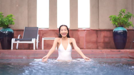 A-pretty-woman-in-the-shallow-end-of-an-indoor-pool-playfully-splashes-water-toward-the-camera