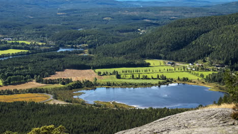 Time-lapse-shot-of-cloud-shadows-moving-over-a-pond-fields-and-forest,-high-up-from-a-mountain,-sunny-day,-in-South-Norway