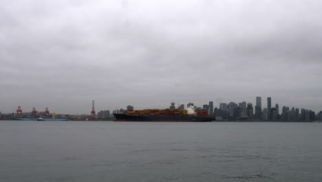 Boote-Segeln-Im-Hafen-Von-Vancouver-Vorbei-An-Einem-Containerschiff,-Das-An-Einem-Bewölkten-Tag-In-Kanada-Im-Hafen-Vor-Anker-Liegt---Totale,-Zeitraffer