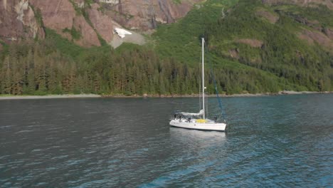 Aerial-View-of-Sailing-Boat-in-Calm-Water-by-Scenic-Alaskan-Coastline,-Drone-Shot