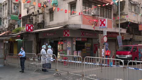 Gesundheitspersonal-In-Pinkelnden-Anzügen-Und-Ein-Polizist-Stehen-Wache-Vor-Einer-Barriere-In-Einem-Gebiet,-Das-Gesperrt-Ist,-Um-Die-Ausbreitung-Des-Ausbruchs-Der-Coronavirus-Variante-In-Hongkong-Einzudämmen