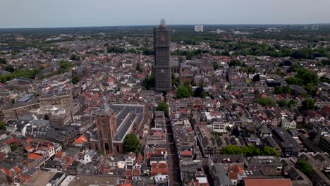 Panoramic-aerial-approach-of-De-Dom-medieval-cathedral-tower-in-scaffolding-in-Dutch-city-center-of-Utrecht-towering-over-the-cityscape-against-a-blue-sky-sunrise-and-orange-glow-on-the-horizon