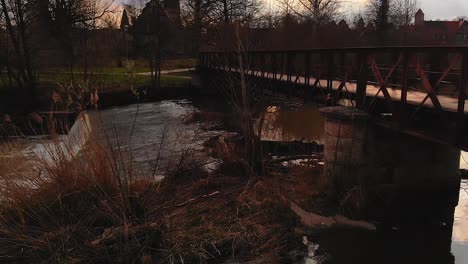 Eine-Drohne-Erhebt-Sich-über-Den-Fluss-Und-Passiert-Die-Brücke-Im-Stadtpark