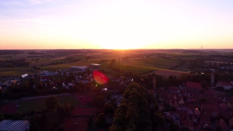 Luftdrohne-Fliegt-Gegen-Den-Sonnenuntergang-Schönes-Panorama-Der-Altstadt-Fußballplatz-Bäume-Parken-Grüne-Wiesen-Und-Felder-Linseneffekt
