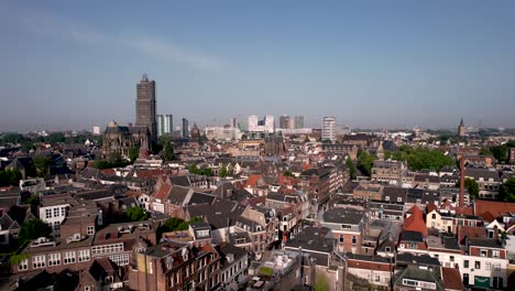 Aerial-view-of-De-Dom-medieval-cathedral-tower-in-scaffolding-in-Dutch-city-center-of-Utrecht-towering-over-the-cityscape-against-a-blue-sky-downward-reveal-of-tree-and-city-park-with-fountain