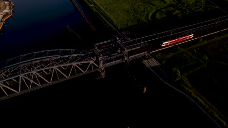 Seitliche-Luftschwenkung-Mit-Zugbrücke-Aus-Stahl-über-Den-Fluss-Ijssel-Mit-Vorbeifahrendem-Zug-Bei-Sonnenuntergang