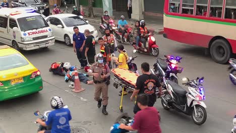 Polizist-Spricht-Mit-Dem-Verletzten-Autofahrer,-Der-Auf-Dem-Boden-Liegt,-Während-Er-Bei-Einem-Motorradunfall-In-Bangsue,-Bangkok,-Thailand-Auf-Die-Trage-Wartet---Hochwinkelaufnahme