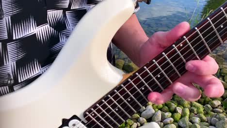 a-male-guitarist-plays-a-white-guitar-by-the-lake