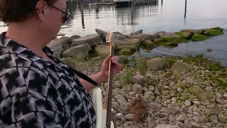 a-man-playing-guitar-on-the-shore-of-the-lake