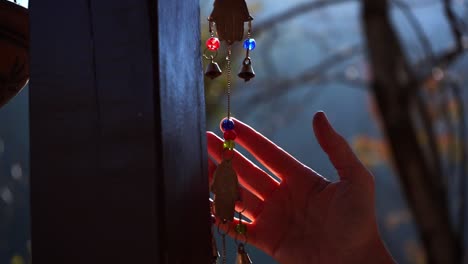 Hand-Touching-Colorful-Metal-Wind-Chime-Hanging-By-A-Wooden-Column