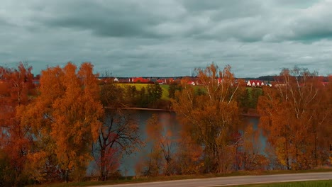 Ein-Panorama-Bewölkter-Himmel-Rote-Dächer-Einer-Kleinstadt-Wiese-Und-Schöne-Bäume-Mit-Herbstfarben-Entlang-Des-Sees