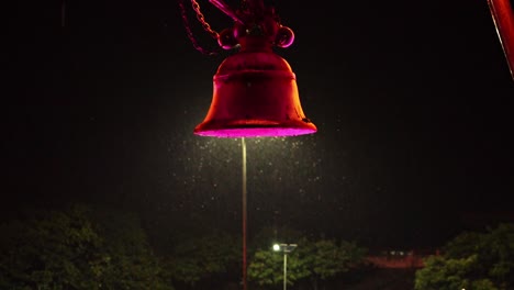 Swarm-Of-Insects-Flying-Around-A-Colorful-Glowing-Bell-On-A-Rainy-Night---close-up