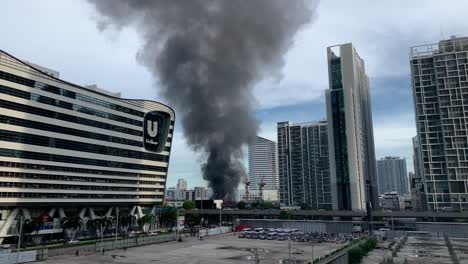Thick-Black-Smoke-Rising-Up-To-The-Sky-From-A-Burning-Building-In-Rama-IX-Road,-Huang-Khwai,-Bangkok,-Thailand-Near-Unilever-House-Building-At-Daytime---wide-shot