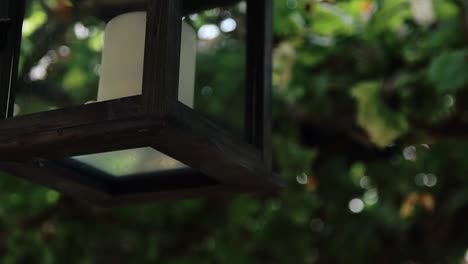 on-the-porch-hangs-a-lantern-with-a-candle-on-the-background-of-a-vine-with-thick-green-leaves