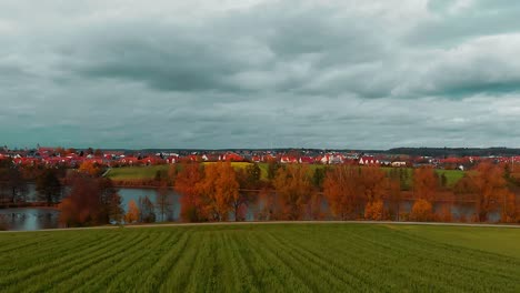 Schönes-Panorama,-Das-Blauen-Bewölkten-Himmel,-Landhäuser-Mit-Roten-Dächern,-See-Mit-Herbstbäumen-Und-Schöne-Farben-Der-Grünen-Wiese-Umfasst