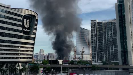 Burning-Building-With-Black-Smoke-Rising-Near-Unilever-Along-Rama-IX-Road,-Huai-Khwang,-Bangkok,-Thailand---wide-shot