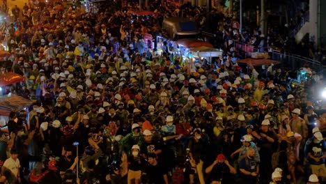 Protesters-Wearing-Hard-Hats-Marching-In-The-Street-In-Bangkok,-Thailand-At-Night---high-angle-shot