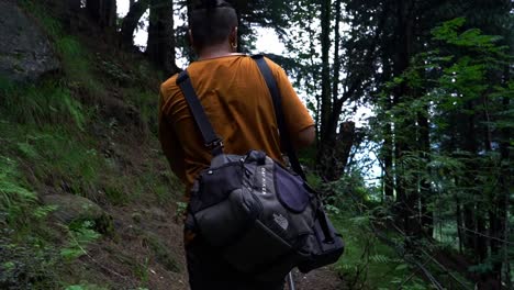 View-Behind-A-Male-Hiker-With-Bags-Walking-Up-On-The-Forest-Trail-In-The-Mountain---slow-motion