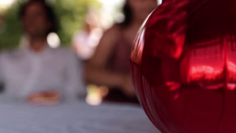 Ein-Roter-Ballon-Der-Hochzeitsfeier-Auf-Dem-Tisch-Im-Hintergrund-Sind-Silhouetten-Von-Menschen-Sichtbar