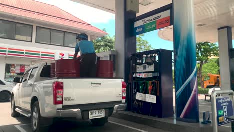 Benzinjunge-Lädt-Petroleum-In-Rote-Metallfässer-Auf-Der-Rückseite-Eines-Isuzu-Dmax-Autos-An-Der-Tankstelle-In-Bangkok,-Thailand---Volle-Aufnahme