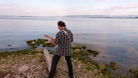 a-man-playing-white-guitar-on-the-shore-of-the-lake