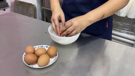 Pastry-dessert-making-in-progress,-patissier-cracking-eggs-into-bowl-commercial-restaurant-setting