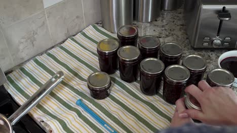 Putting-the-lids-and-seals-on-fresh-homemade-jars-of-berry-jam---over-the-shoulder-view
