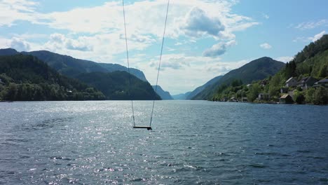 Tall-swing-moving-slowly-from-side-to-side-with-amazing-scenic-Veafjorden-in-background---Static-aerial-with-swing-close-to-fjord-surface---Norway