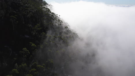 A-drone-shot-of-a-mountain-rising-through-a-thick-cloud