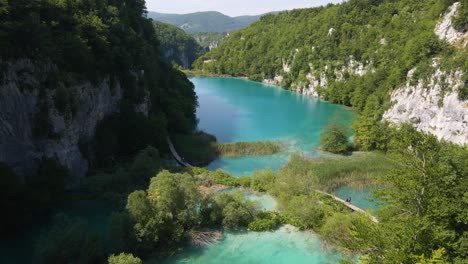 Top-view-of-the-beautiful-Plitvice-Lakes-National-Park-with-many-green-plants-and-beautiful-lakes-and-waterfalls,-as-well-as-the-road-into-the-gorge-along-which-people-go