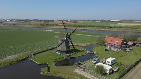 Iconic-Dutch-Windmill-spinning-on-sunny-day-in-rural-landscape,-aerial