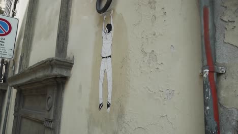 Hanging-man-graffiti-on-old-historic-building-on-street-in-Florence,-Italy