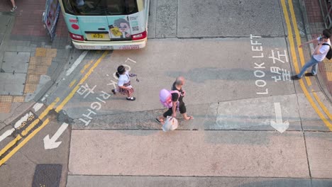 Chinese-pedestrians-and-commuters,-including-a-school-girl,-cross-a-road-after-a-vehicle-drives-by-in-Hong-Kong