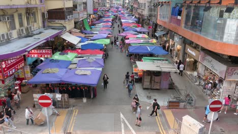 Eine-Weite-Hochsichtaufnahme-Von-Käufern,-Die-Durch-Die-Marktstände-Der-Fa-Yuen-Street-Im-Freien-Gehen-Und-In-Hongkong-Gemüse,-Obst,-Geschenke-Und-Modewaren-Verkaufen