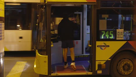 Mann-Wartet-An-Bushaltestelle-Und-Spricht-Mit-Busfahrer-In-Dunklem,-Schmuddeligem-Verkehrsknotenpunkt,-Schlechte-Beleuchtung