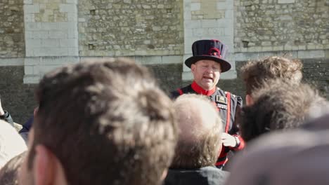 London-city-tour-guide-with-traditional-outfit-explaining-historical-facts-for-tourists-in-the-Tower-of-London,-Yeoman-in-action